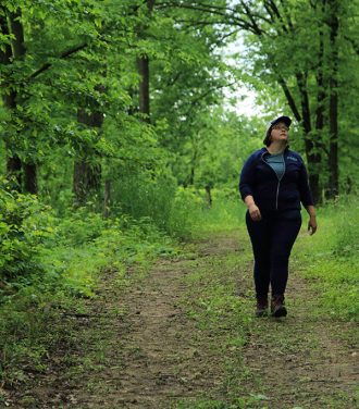 Devon Brock-Montgomery (water quality program manager) walks along wooded road at Savanna Institute's Hillside Farm, Spring Green, Wisconsin.